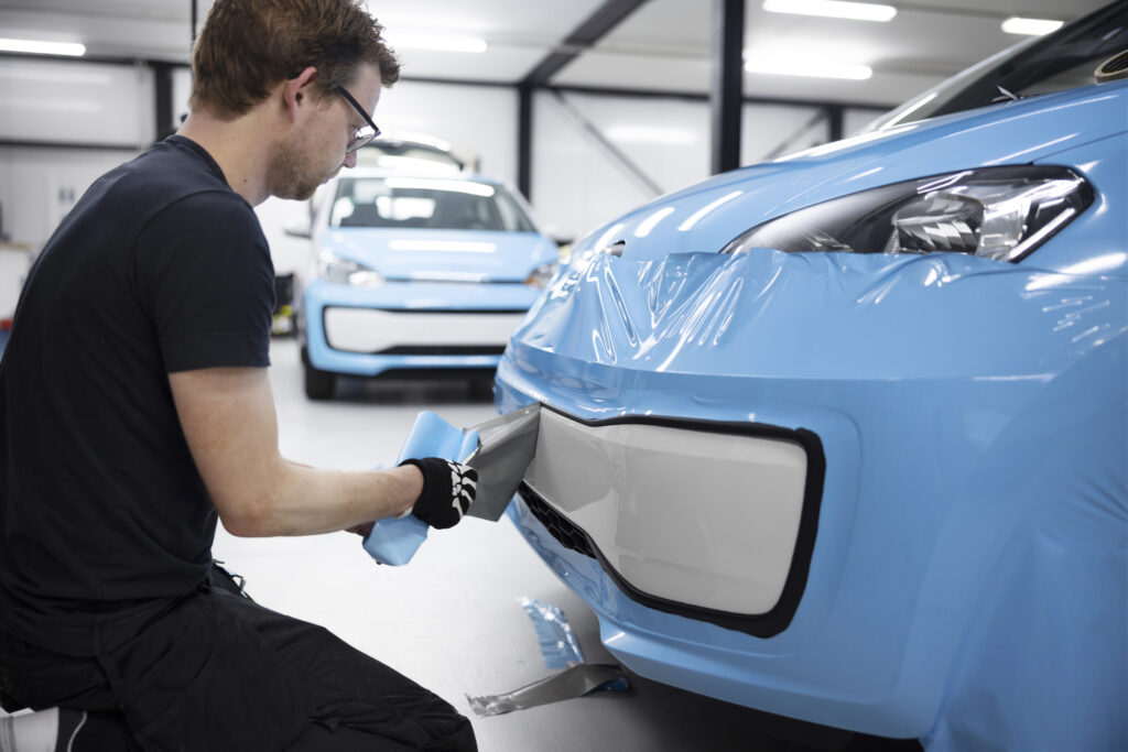 Mechaniker bringt eine Schutzfolie an der Frontpartie eines blauen Autos in einer Werkstatt an