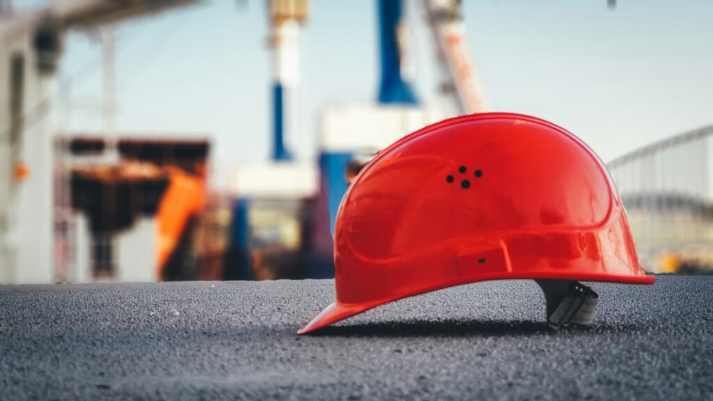 Roter Schutzhelm auf einer Oberfläche vor einer industriellen Kulisse